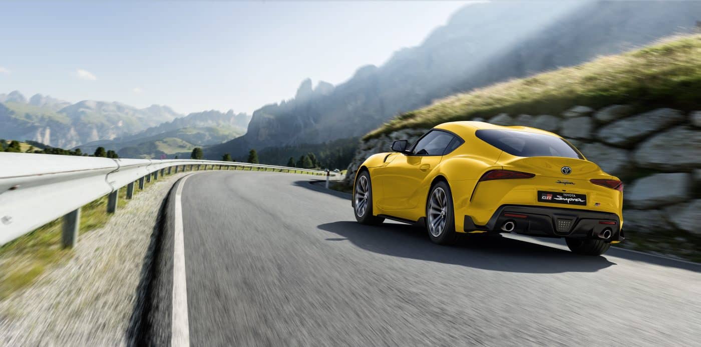 Toyota GR Supra en color amarillo transitando por una carretera, mostrando su silueta trasera y lateral.