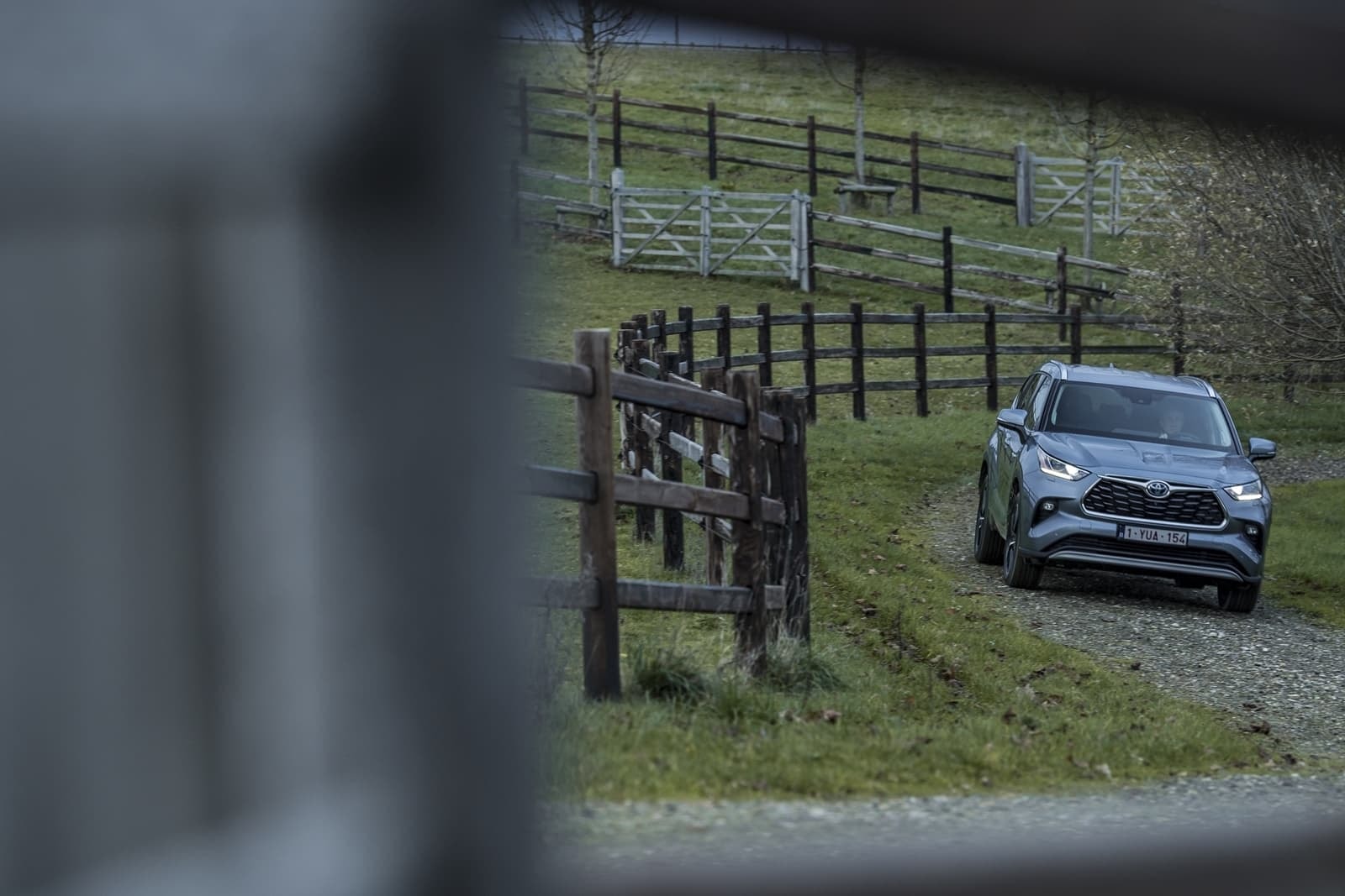 Vista lejana del Highlander híbrido a través de una cerca, ambiente rústico.