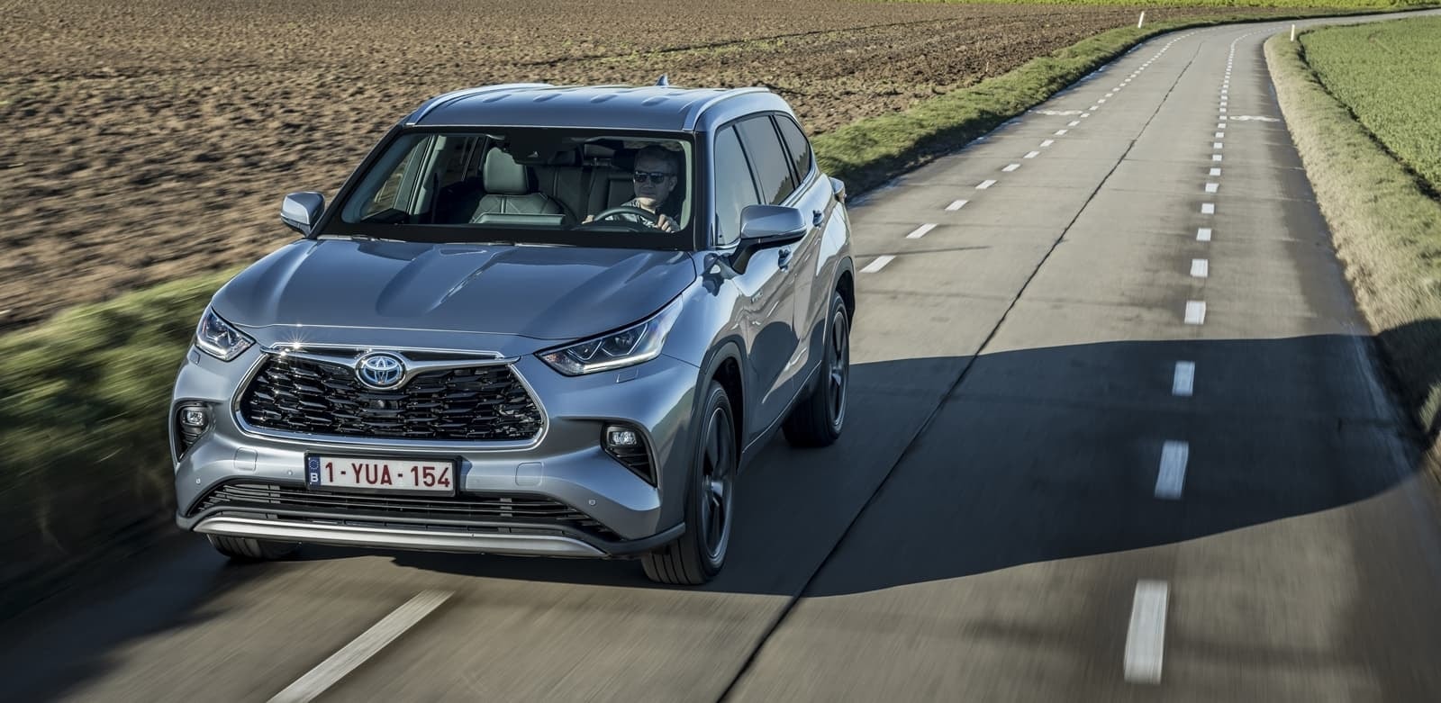 Conductor al volante del Highlander en carretera, desde una perspectiva frontal y lateral.