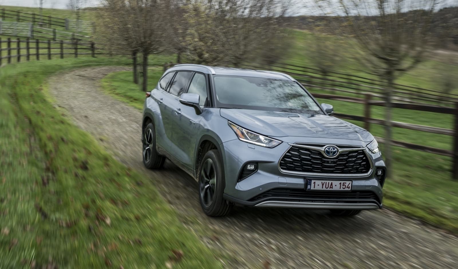Toyota Highlander híbrido en carretera rural, vista lateral y delantera.