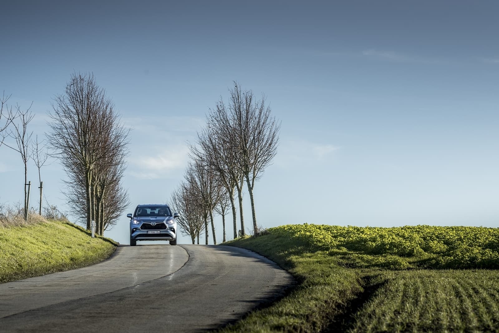 Vista trasera del Highlander Híbrido destacando sus ópticas y diseño en un camino rural.