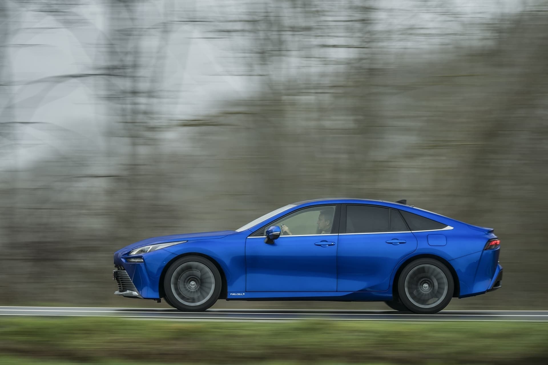 Perfil lateral del Toyota Mirai azul en movimiento por una carretera.