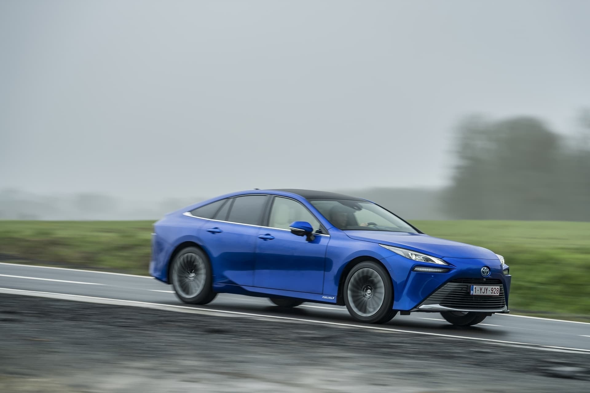 Perfil lateral del Mirai cruzando un entorno rural y sereno.