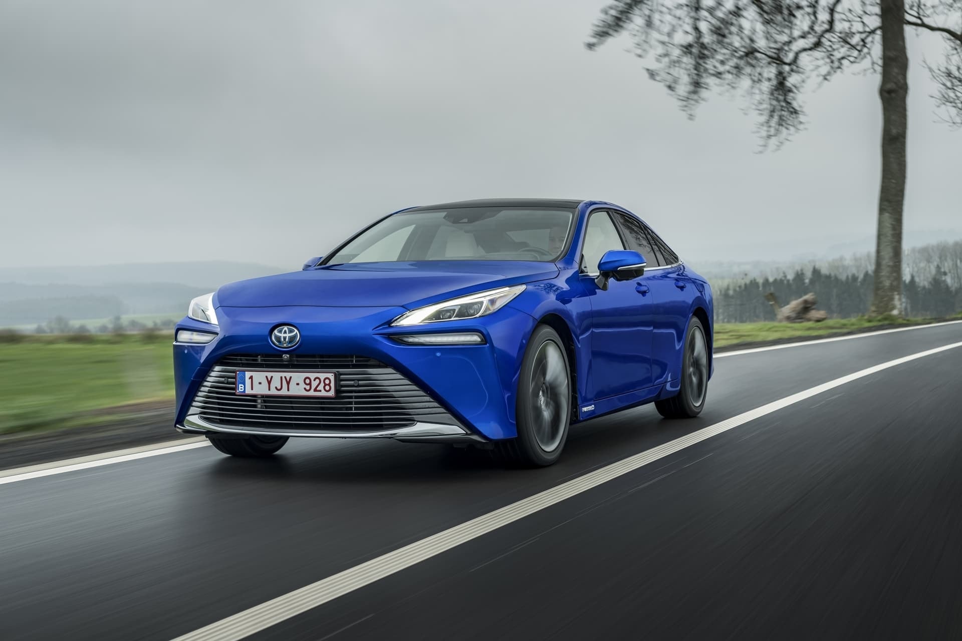 Frente del Toyota Mirai navegando por la carretera, diseño agresivo y moderno.