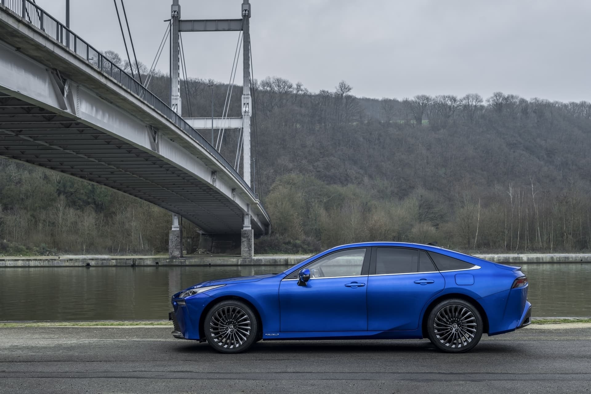 Lateral del Toyota Mirai con imponente puente al fondo, diseño elegante.