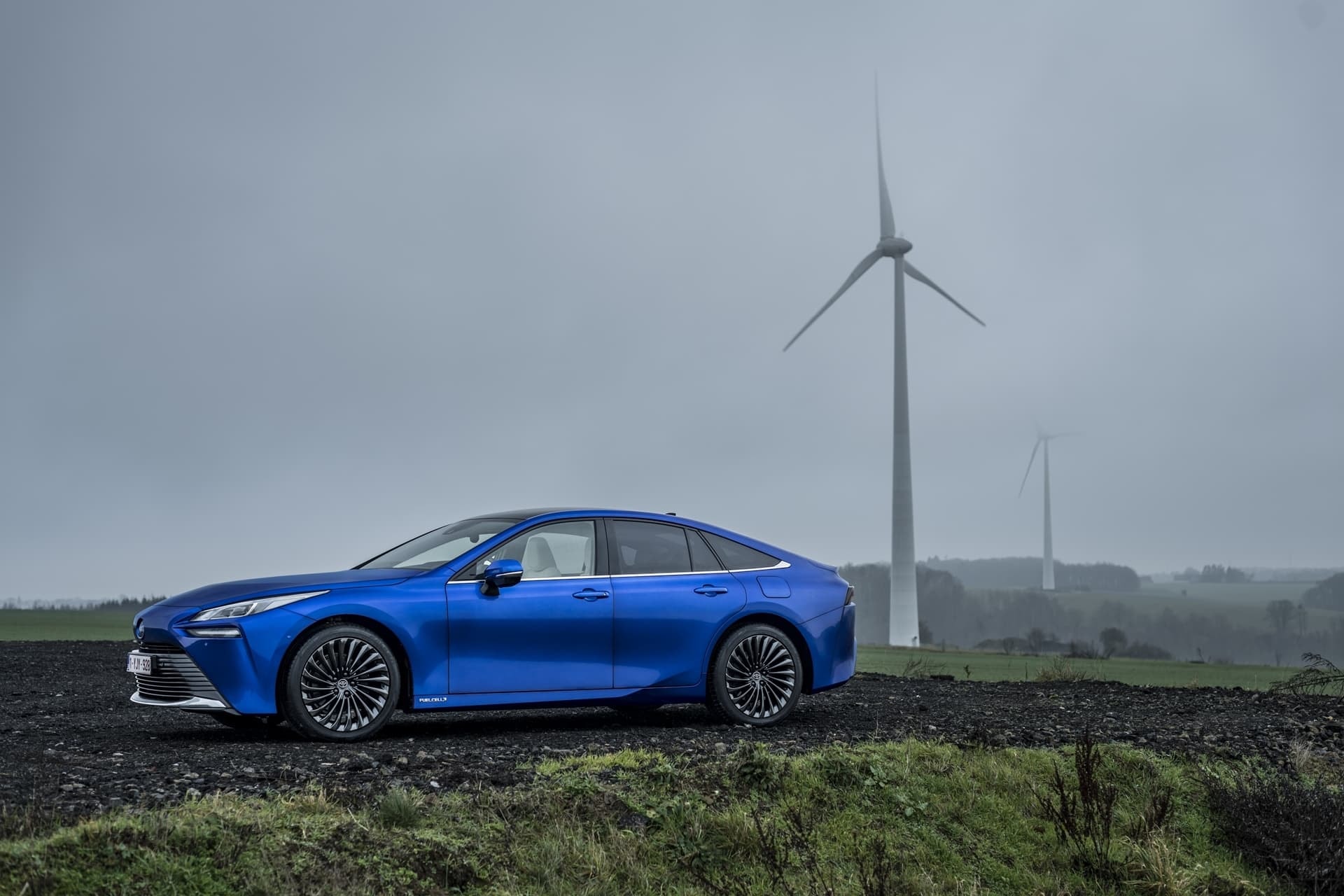 Mirai azul con fondo de turbinas eólicas, resaltando su eco-eficiencia.