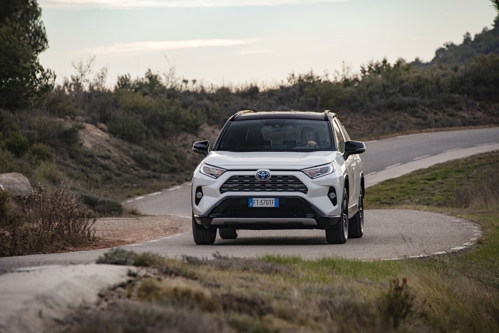 Perspectiva frontal del RAV4 híbrido aproximándose en una curva carretera.