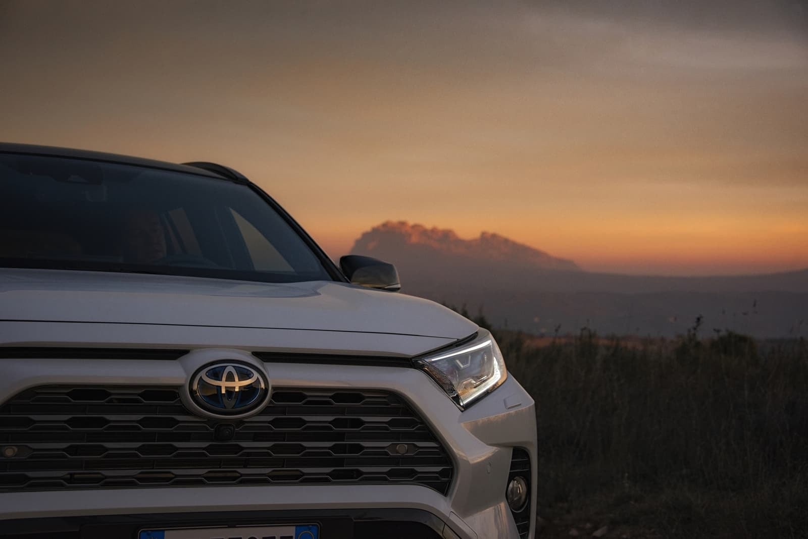 Primer plano del frente del RAV4 híbrido con una suave luz de atardecer, mostrando detalles de su diseño.