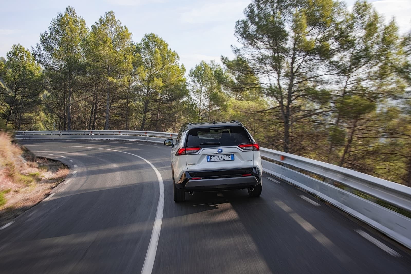 Vista trasera del RAV4 híbrido en acción, mostrando su diseño y capacidad en carretera.