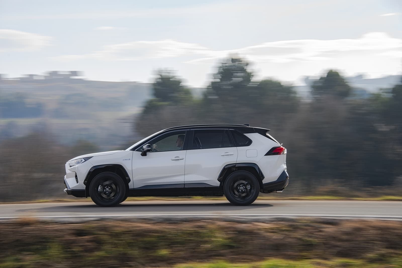 RAV4 Híbrido lado conductor en acción, reflejando su perfil atlético.