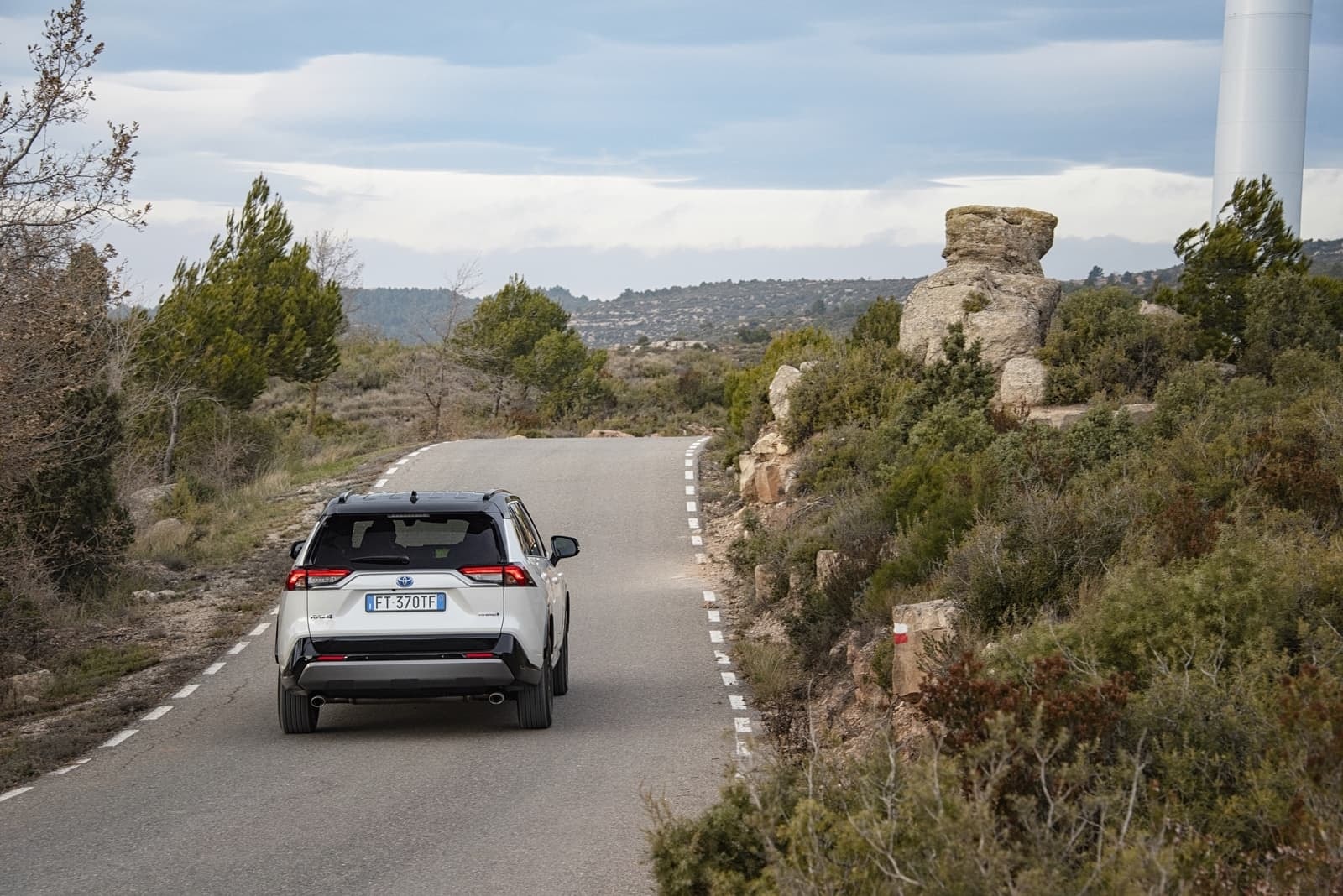 RAV4 Híbrido tomando una curva, vista trasera y paisaje natural.