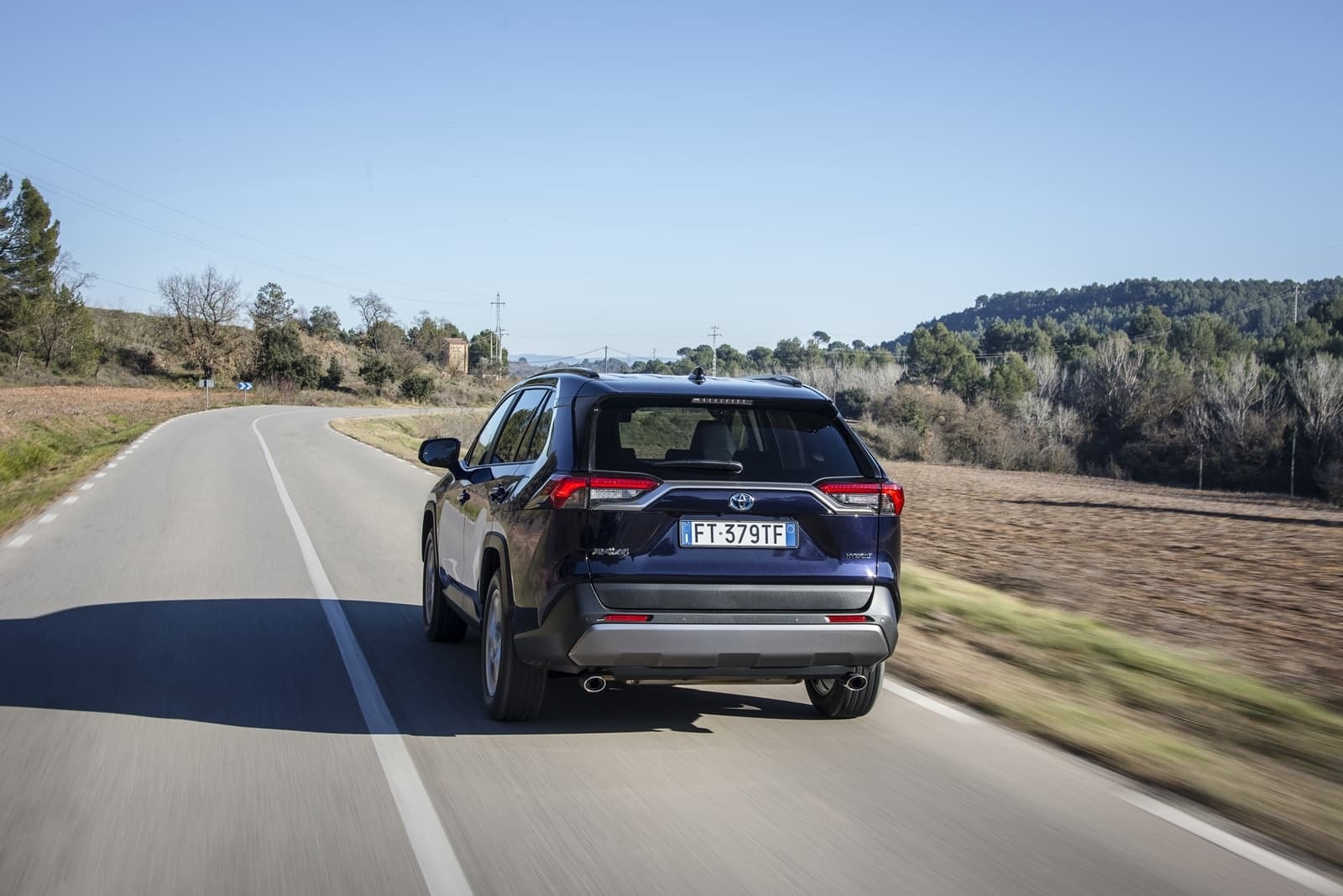 Perspectiva trasera del RAV4 Híbrido en movimiento sobre asfalto.