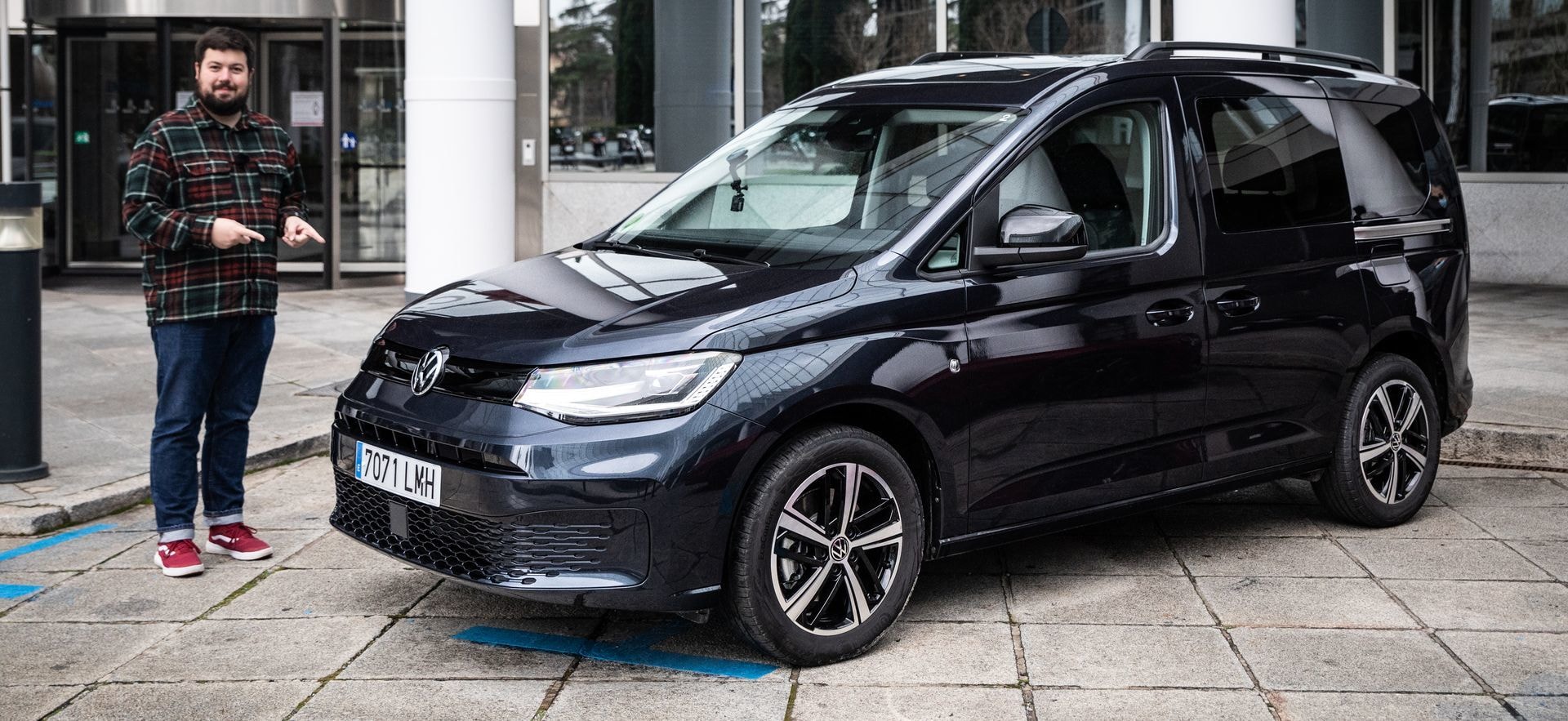 Un hombre parado al lado de un Volkswagen Caddy, destacando su diseño frontal y lateral.
