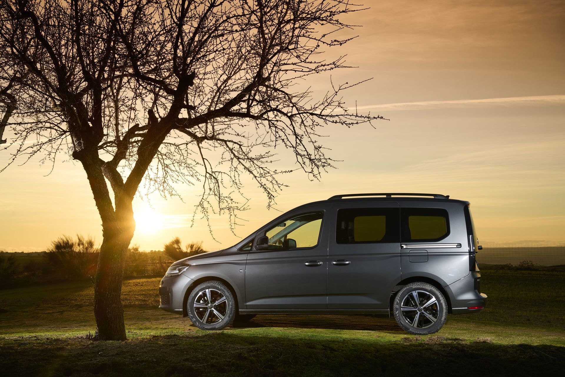 Volkswagen Caddy en perfil lateral con un árbol y el sol de fondo.