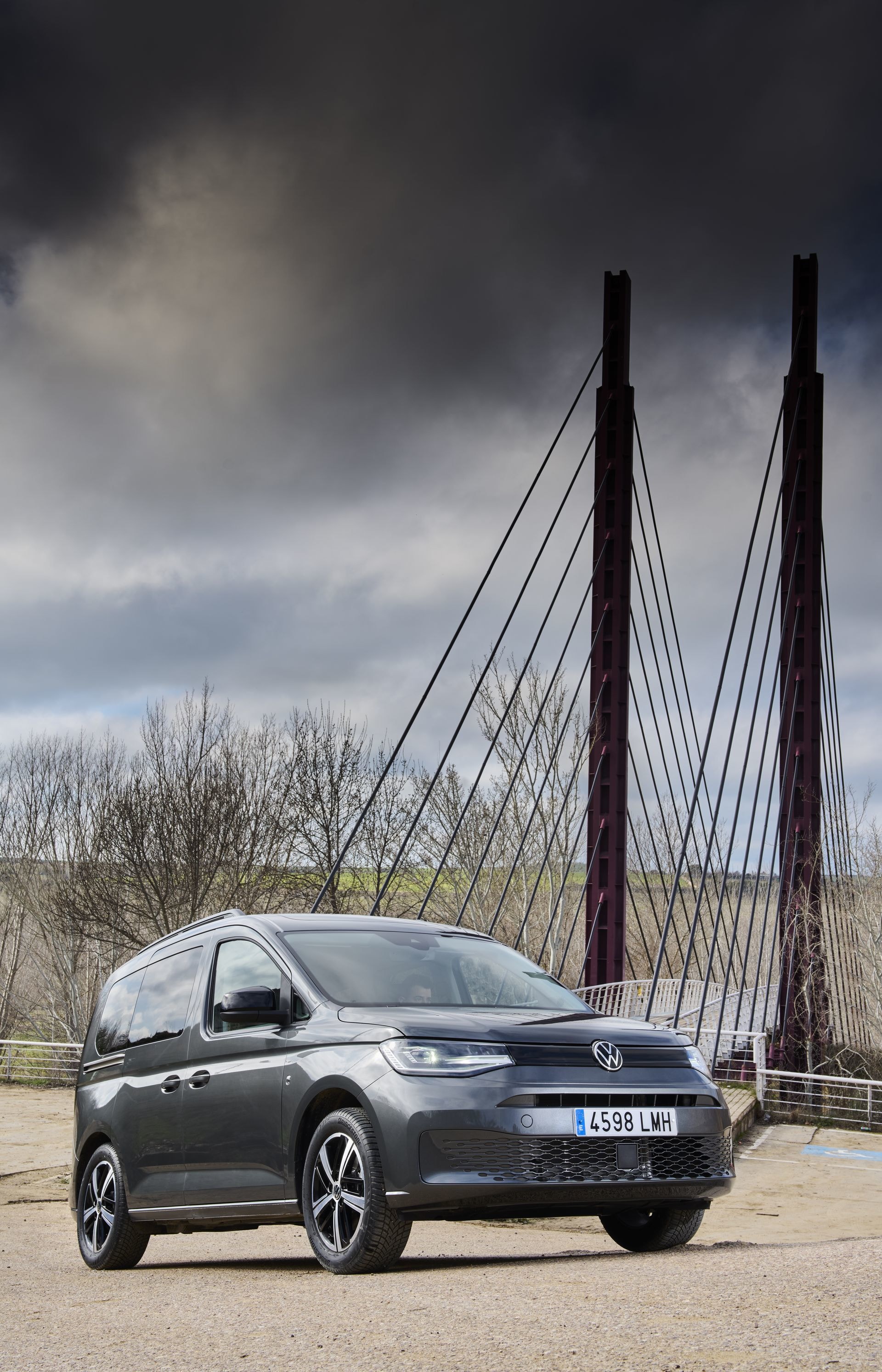 Volkswagen Caddy estacionado lateralmente con un puente de fondo, destacando su silueta.