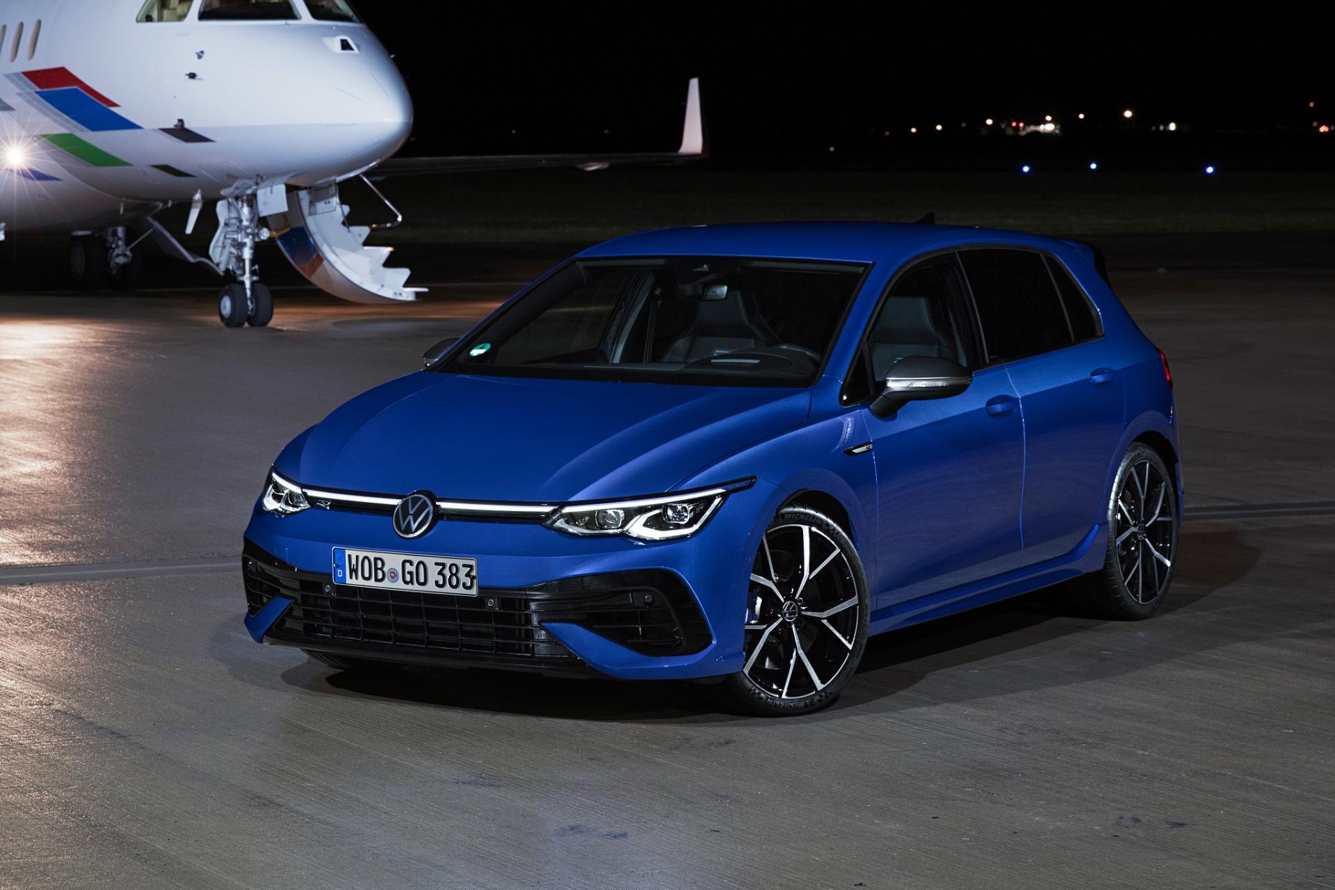 Volkswagen Golf R en azul delante de avión privado.