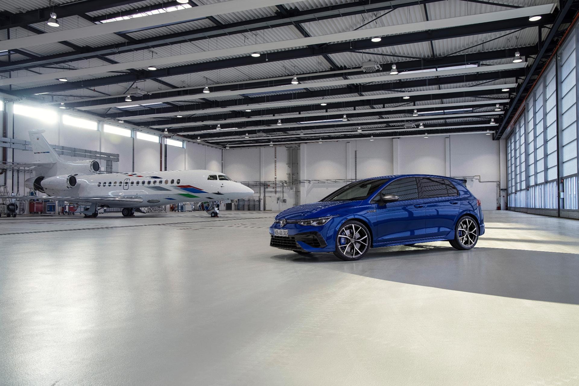 Vista lateral del Golf R en un hangar con avión al fondo, resaltando su diseño deportivo.