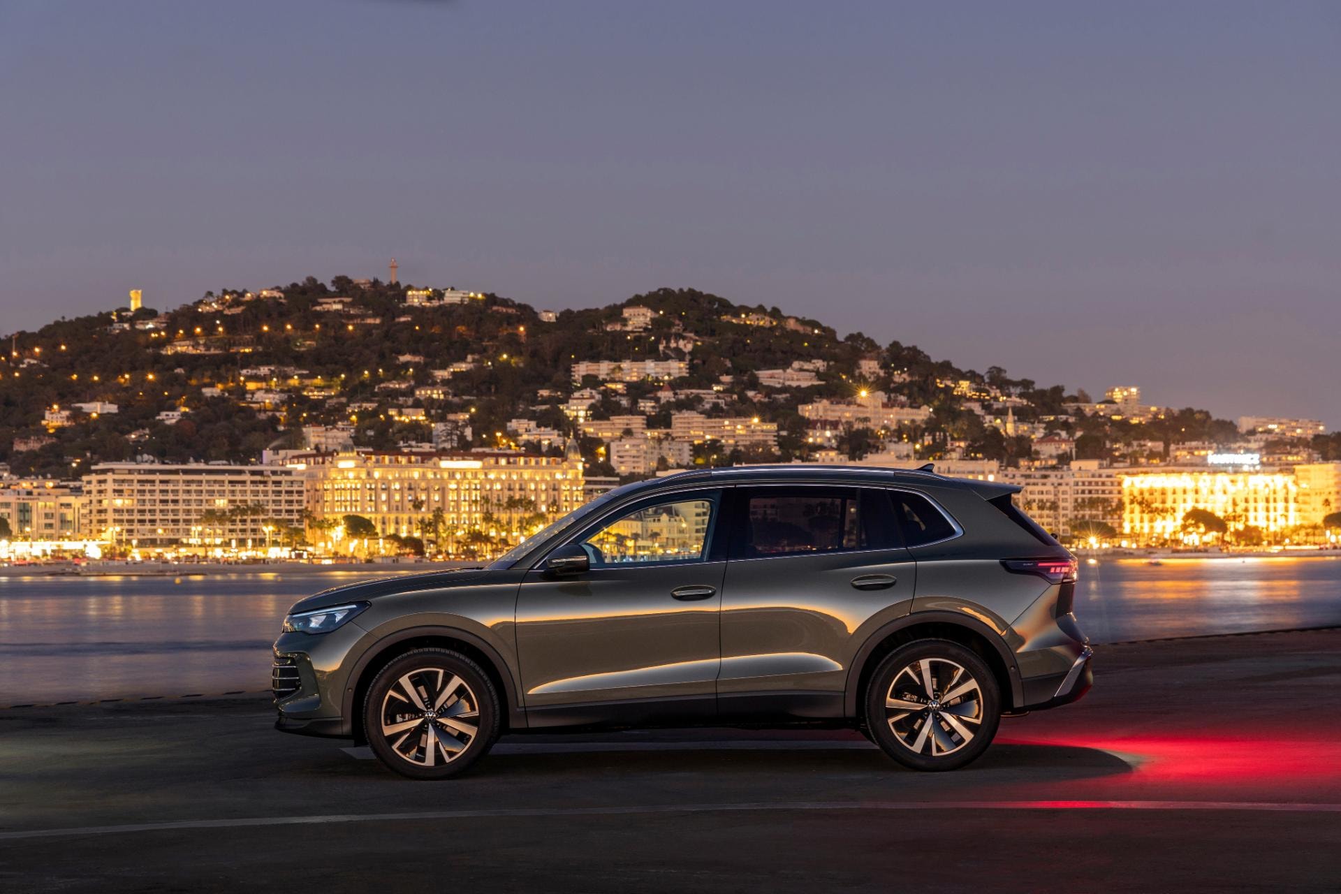 Vista lateral del Tiguan híbrido iluminado por la ciudad al anochecer