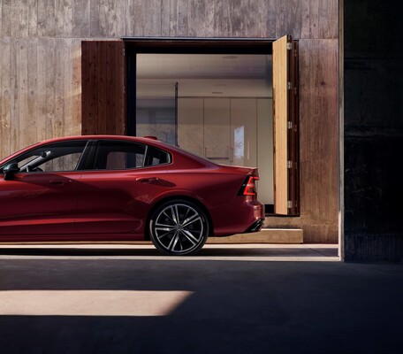 Perfil lateral del Volvo S60 en tono rojo junto a una moderna edificación. Perfil lateral del Volvo S60 en tono rojo junto a una moderna edificación.