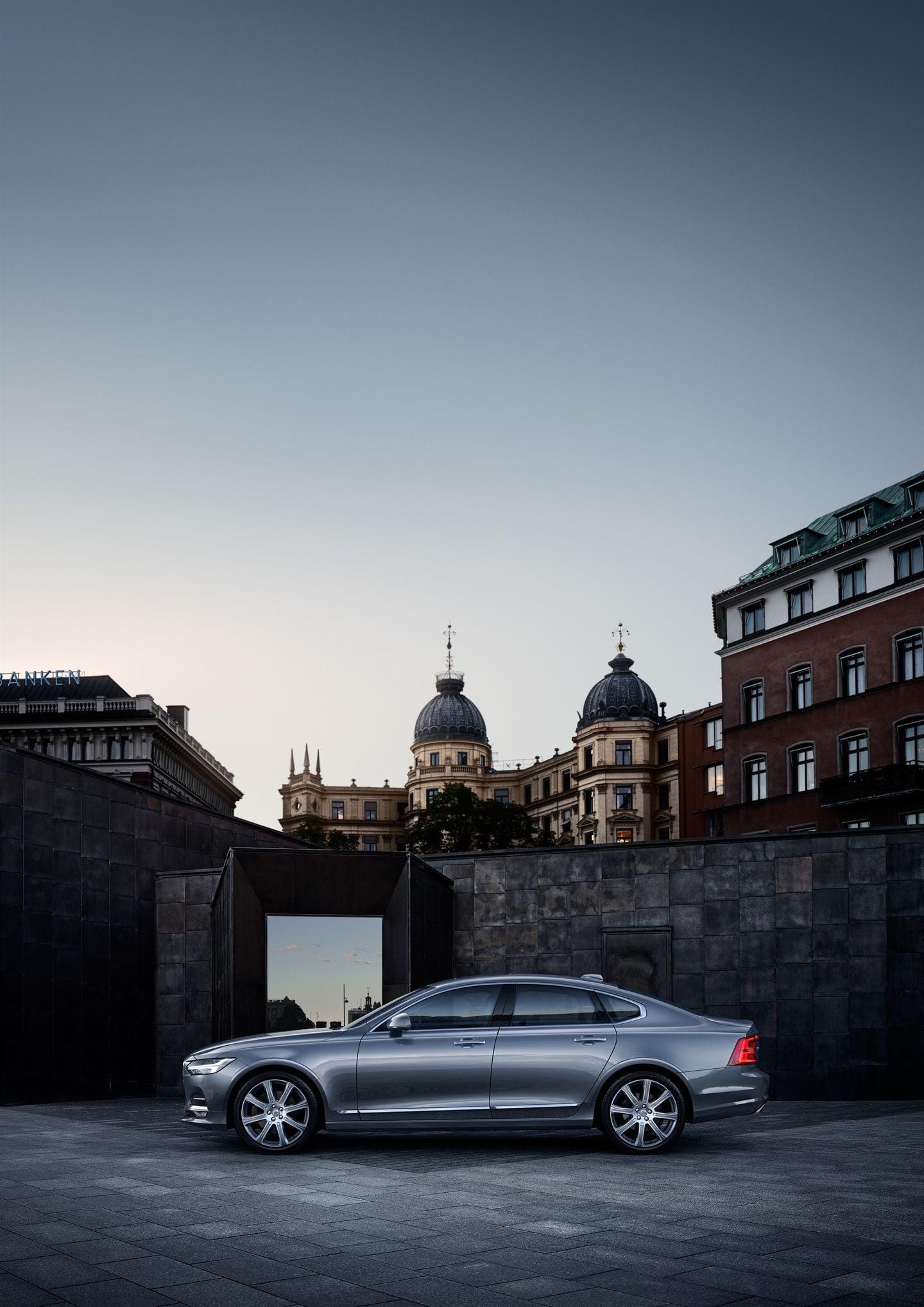 Silueta lateral del Volvo S90 destacando sobre un fondo urbano de edificios históricos.