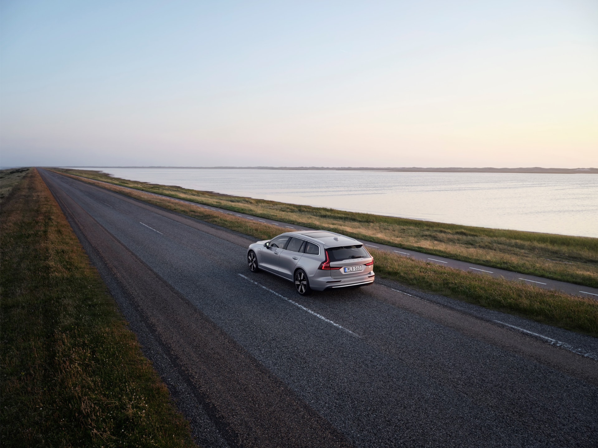 Vista trasera y lateral del Volvo V60 híbrido en un impresionante atardecer en la carretera.