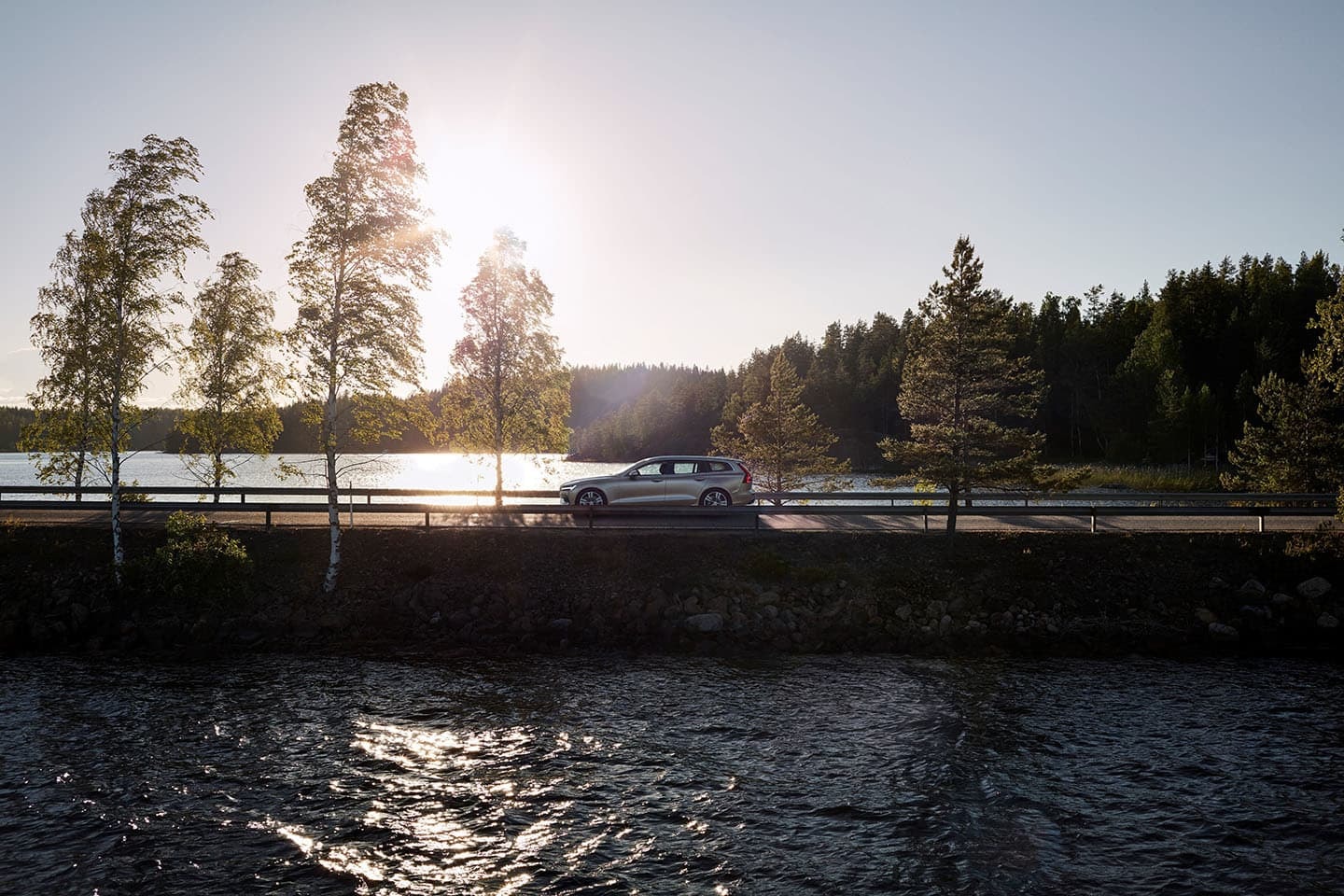 Vista lateral del Volvo V60 en una idílica carretera junto a un río.