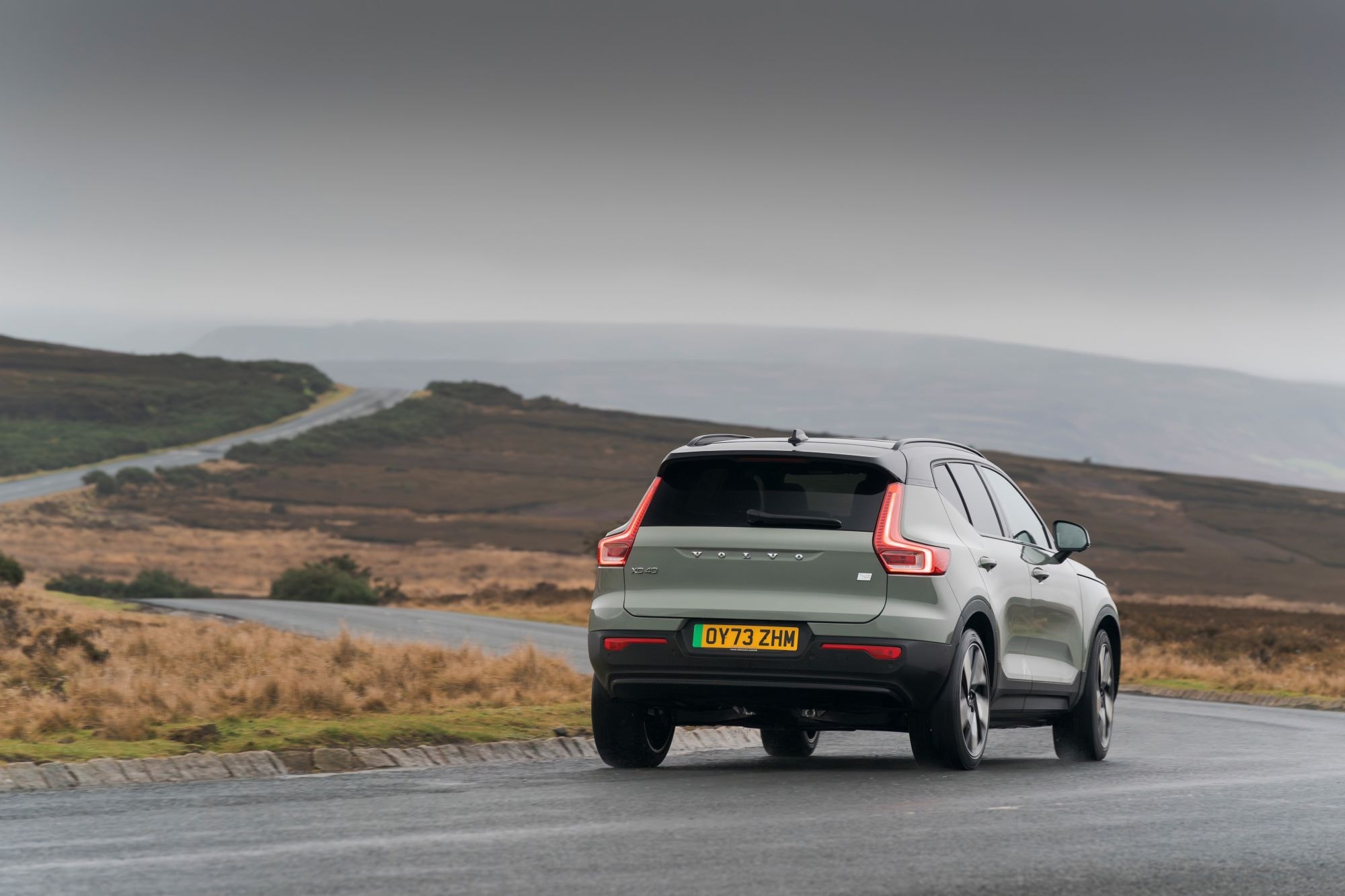 Diseño trasero del Volvo XC40 mientras se desplaza en un entorno rural con niebla.